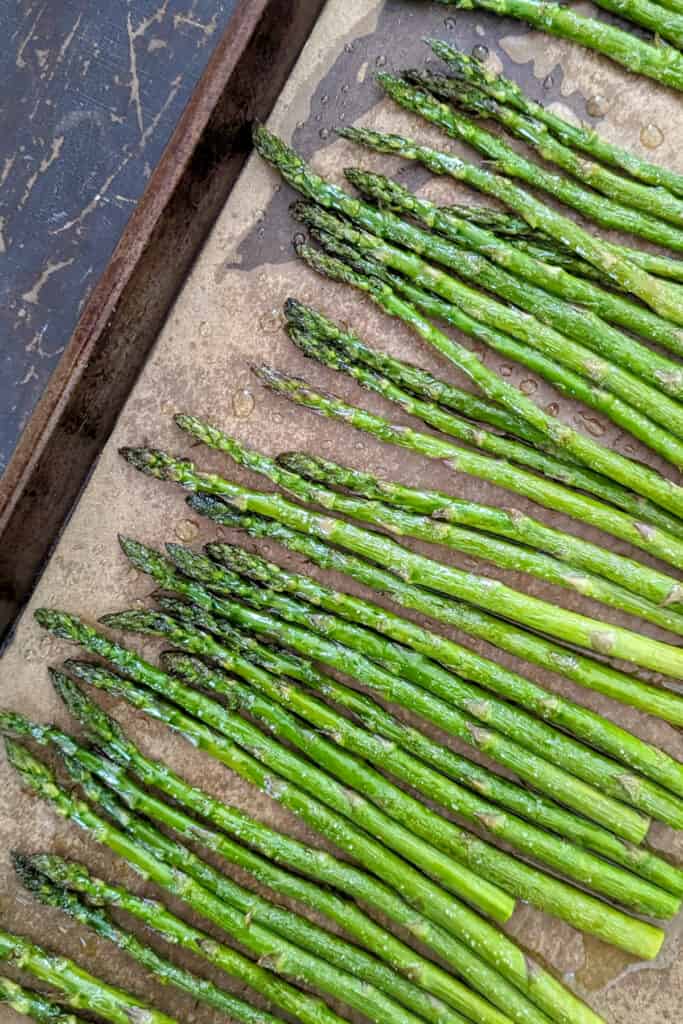 A sheet tray with brown parchment paper and on top is vibrant green roasted asparagus.