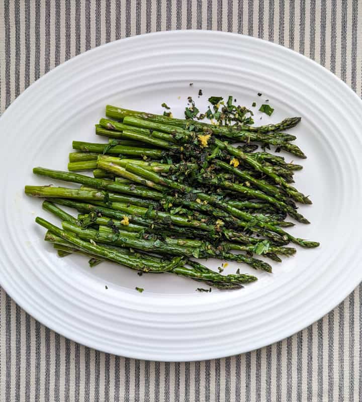 A white platter with roasted asparagus topped with finely chopped mint and parsley, and lemon zest.