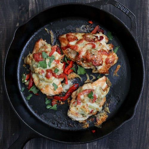 Cast iron skillet with seared chicken breasts topped with artichokes, peppers and cheese.