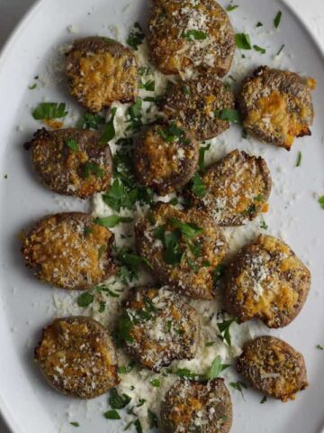 Overhead shot of a white platter with air fryer smashed potatoes topped with chopped parsley and grated parmesan cheese.