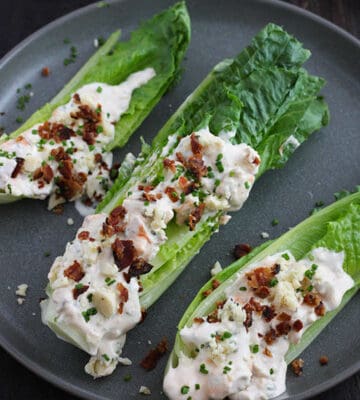A blue plate with wedges of romaine hearts topped with buffalo blue cheese dressing, chopped bacon, crumbled blue cheese and chopped chives.