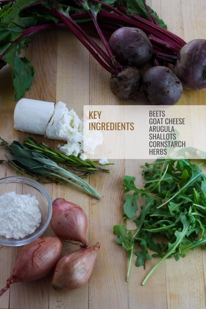 Cutting board with whole purple beets, arugula, shallots, herbs, goat cheese and a small bowl of cornstarch.