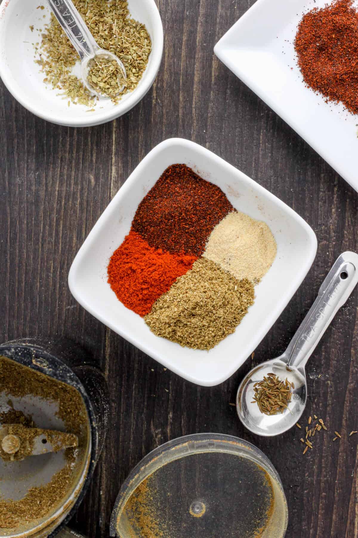 A white bowl with spices and a black spice grinder off center.