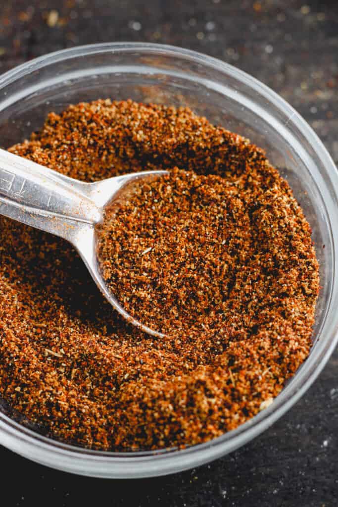 A clear bowl with chicken taco seasoning and a teaspoon.