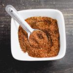 A white bowl with chicken taco seasoning and a teaspoon.