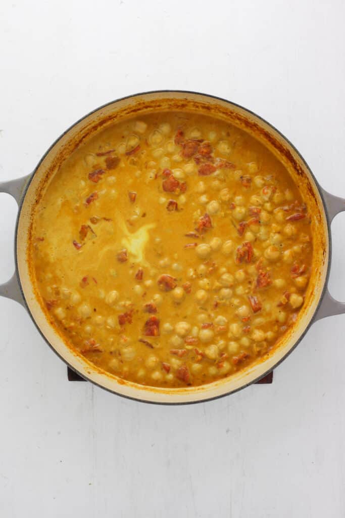 A braiser pan with coconut milk, chickpeas, tomatoes and onions.