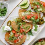 A platter of crispy chicken tacos topped with shredded lettuce and guacamole.
