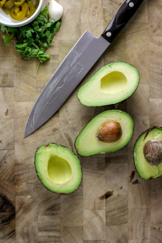 Cutting board with avocadoes cut in half and a chef knife.