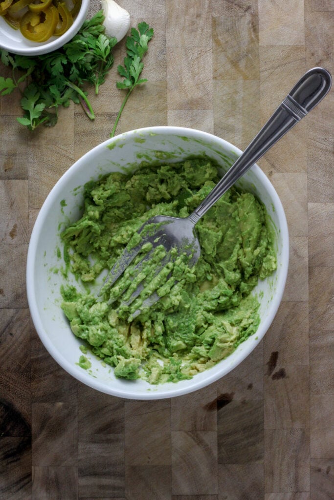 A white bowl with mashed avocado and a fork.
