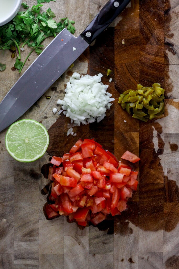 A cutting board with chopped tomatoes, onion and pickled jalapeno.