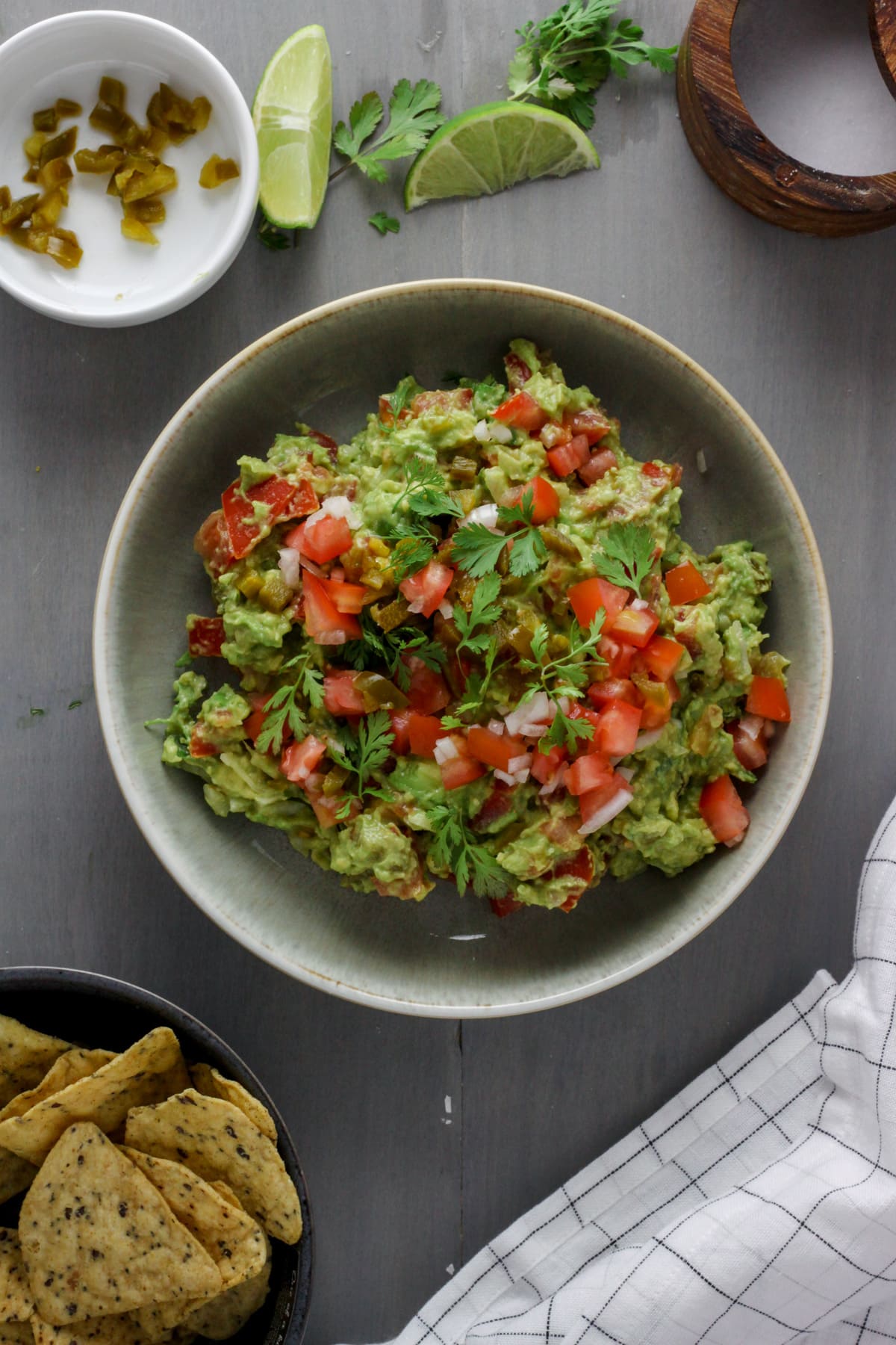 A white bowl with guacamole pico de gallo and tortilla chips on the side.