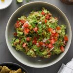 A bowl of guacamole topped with pico de gallo.