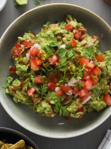A bowl of guacamole topped with pico de gallo.
