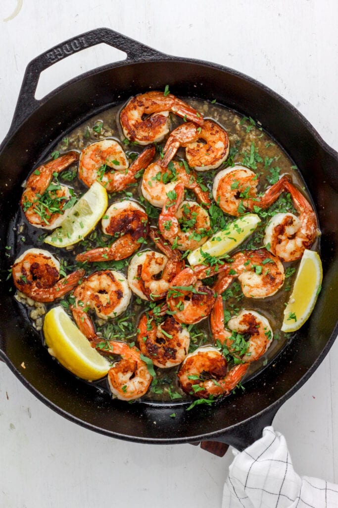 Skillet with seared shrimp, white wine sauce, herbs and lemon wedges.
