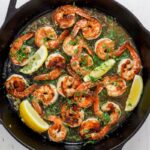 Skillet with seared shrimp, herbs, wine sauce and lemon wedges.