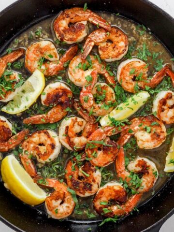 Skillet with seared shrimp, herbs, wine sauce and lemon wedges.