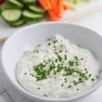 A white bowl of sour cream and chive dip topped with chives.