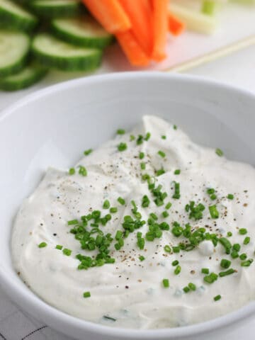 A white bowl of sour cream and chive dip topped with chives.