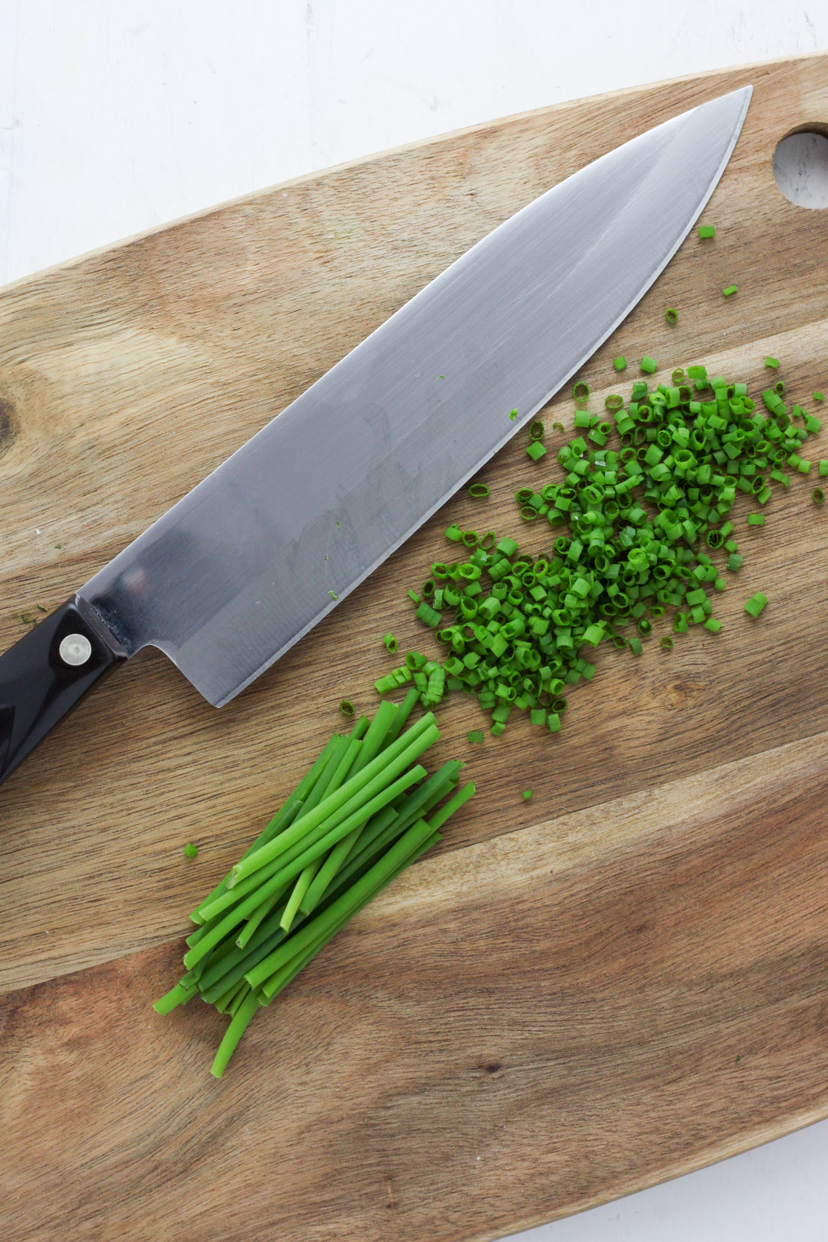 A wooden cutting board with a knife and chopped chives.