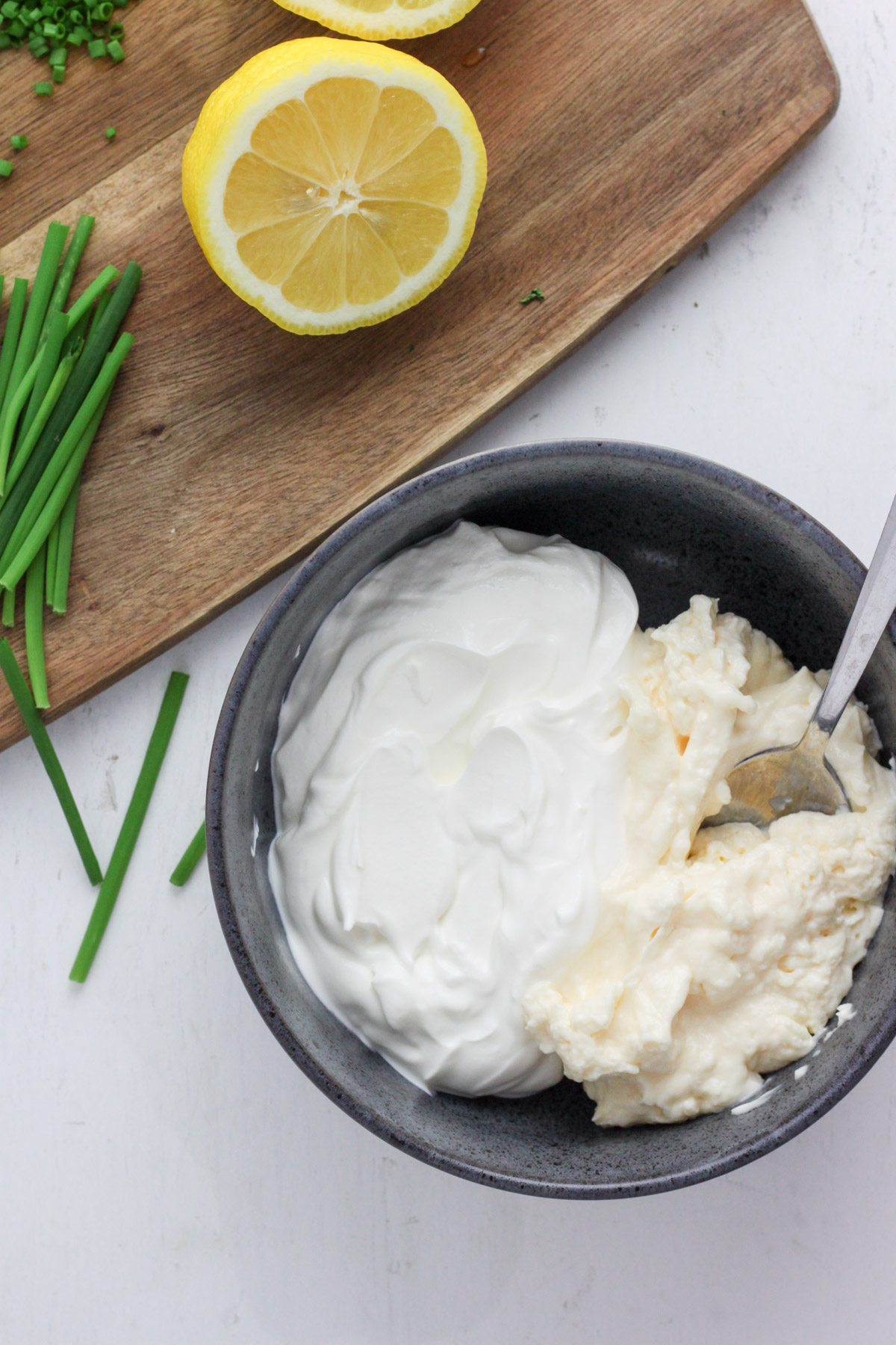 A blue bowl with sour cream and mayonnaise and a cutting board with a lemon.