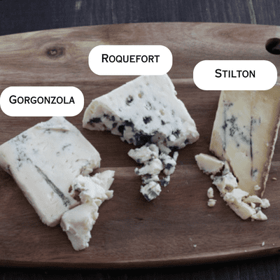 Cutting board with gorgonzola, Roquefort and stilton blue cheeses.