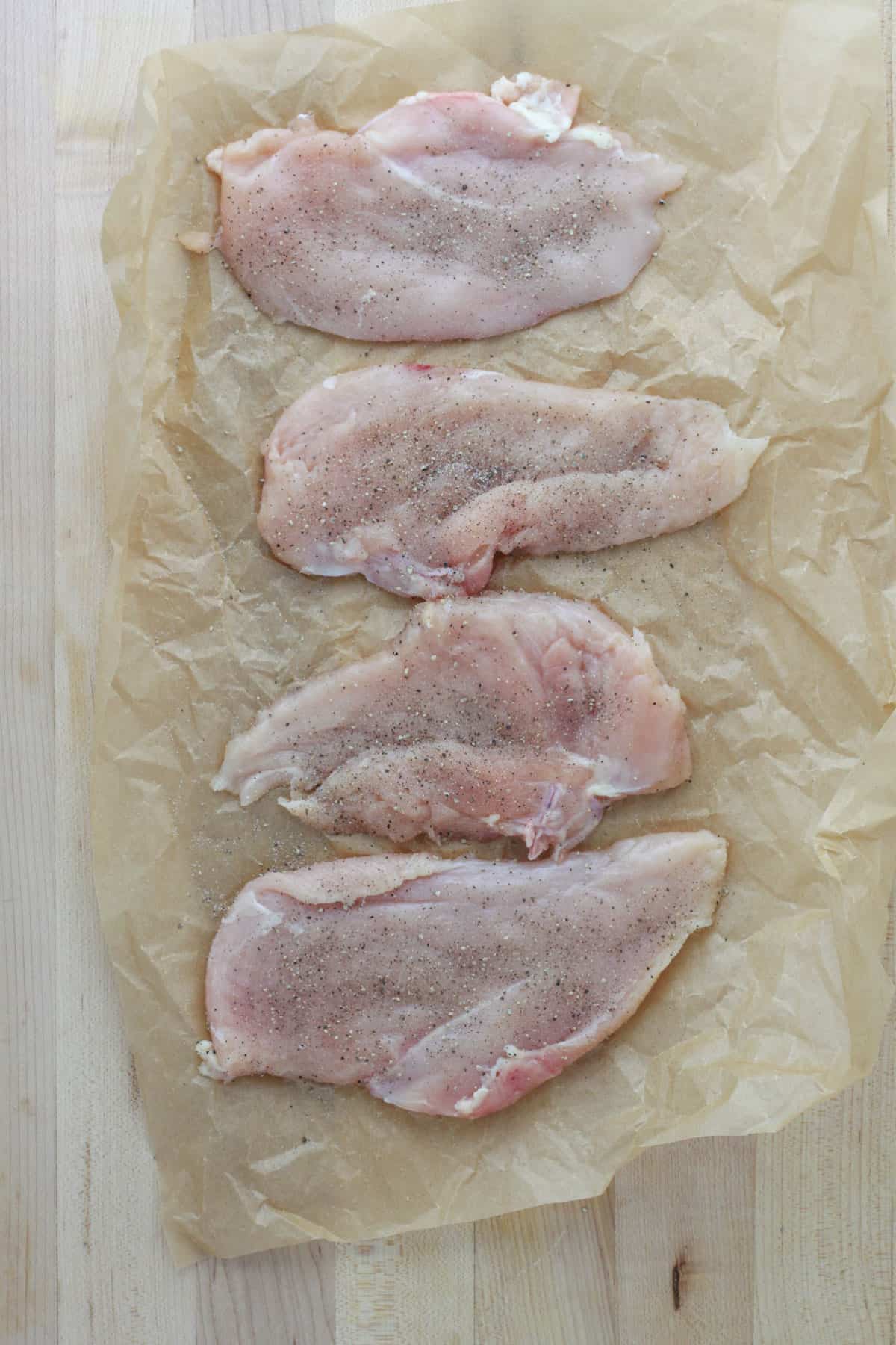 Chicken breasts cut in half crosswise and pounded to a half inch thickness on a piece of parchment paper.