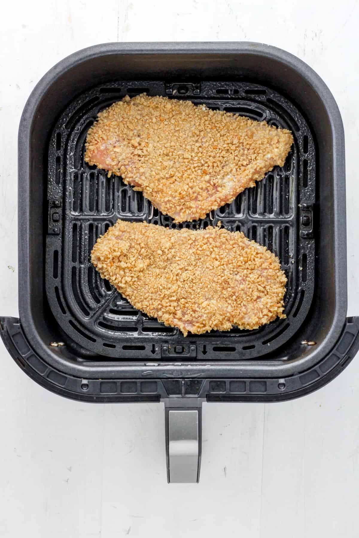 Breaded chicken cutlets uncooked in the basket of an air fryer.