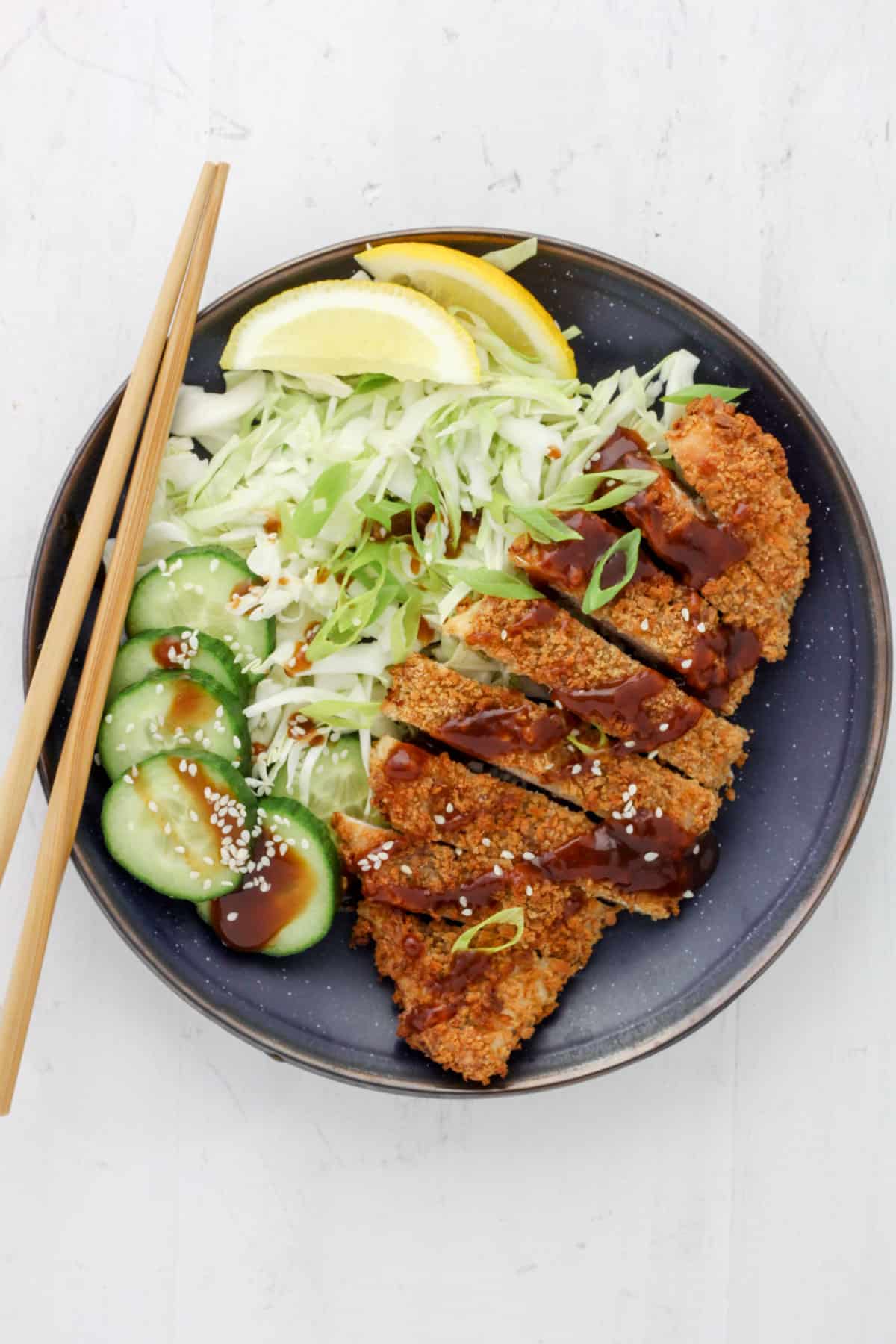 Air Fryer Chicken Katsu with shredded green cabbage, lemon wedges and cucumbers.