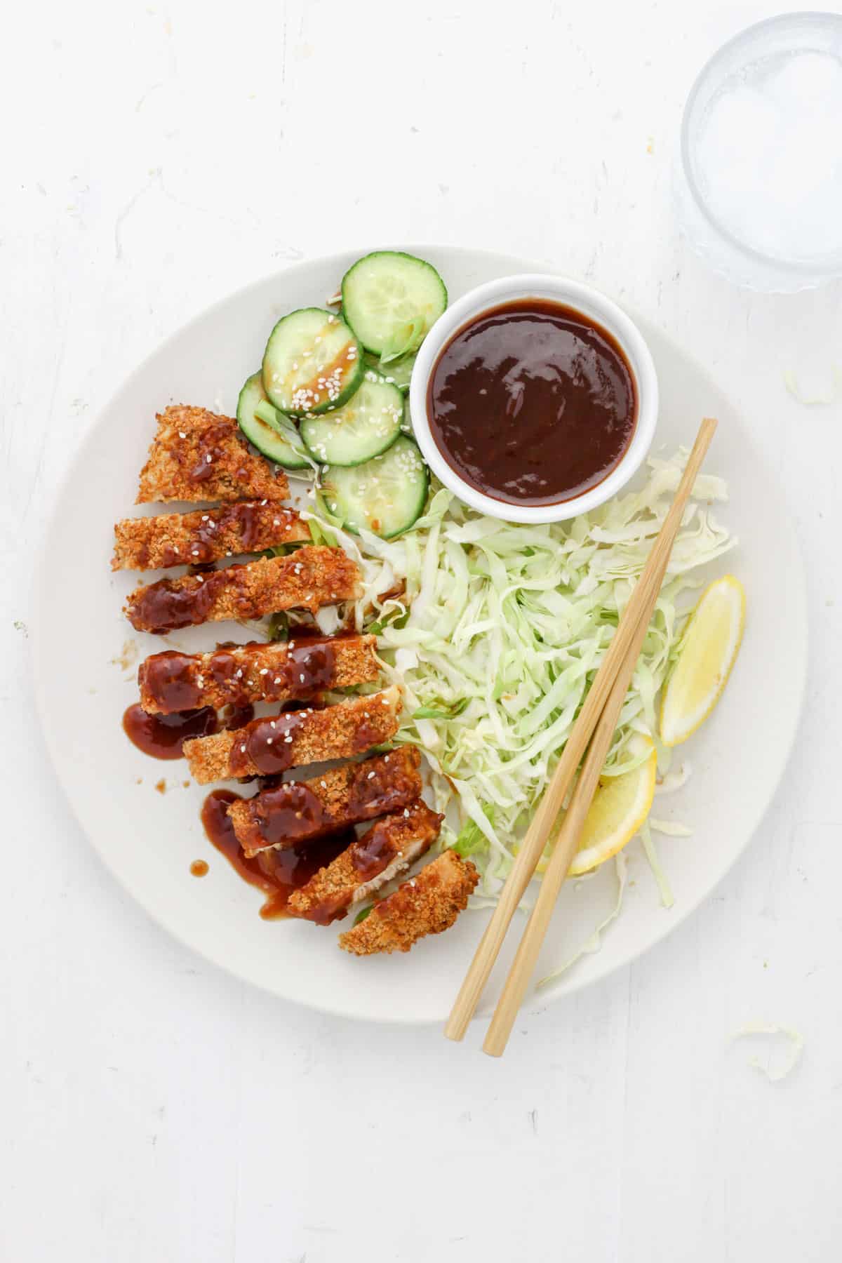 A plate of air fryer chicken katsu topped with homemade tonkatsu with green cabbage and cucumbers.