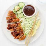 Air Fryer Chicken Katsu with shredded green cabbage, lemon wedges and cucumbers.
