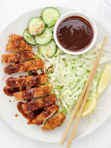 Air Fryer Chicken Katsu with shredded green cabbage, lemon wedges and cucumbers.
