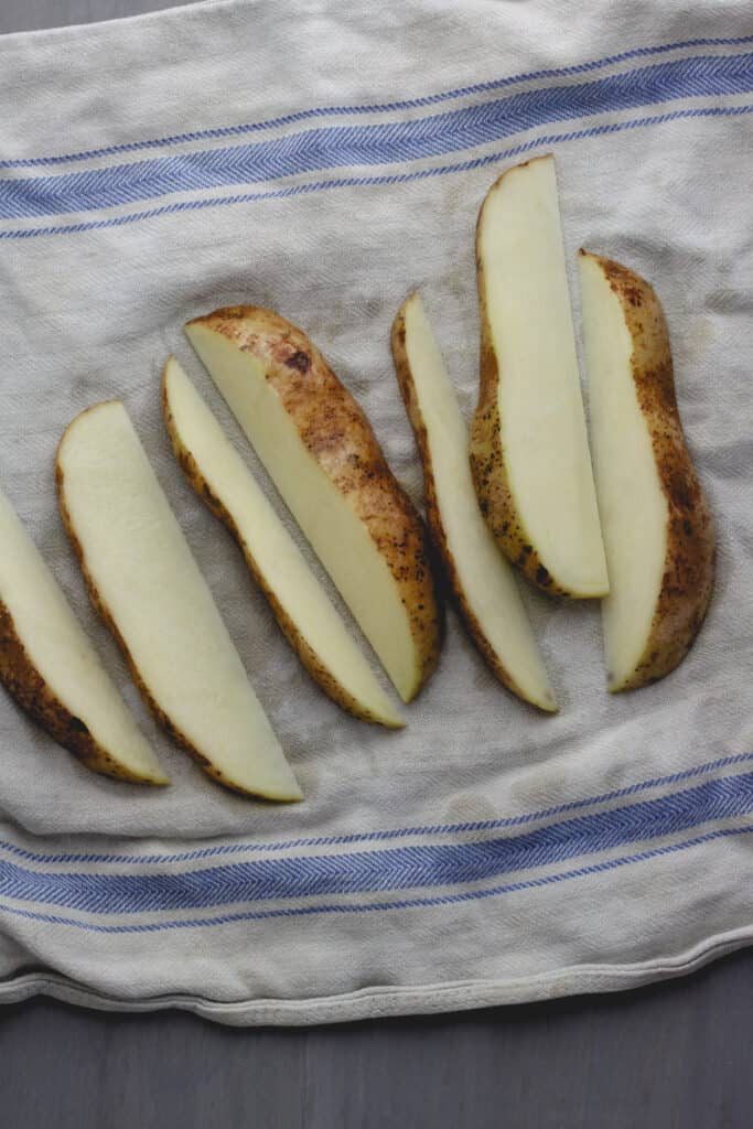 Russet potato wedges drying on a kitchen towel.