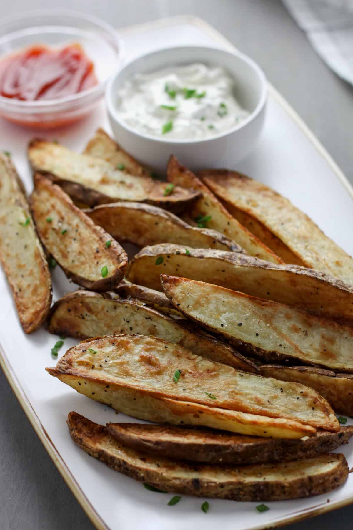 A white platter of air fryer steak fries topped with chives.