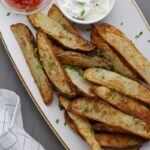 A white platter of crispy air fryer steak fries sprinkled with chives.