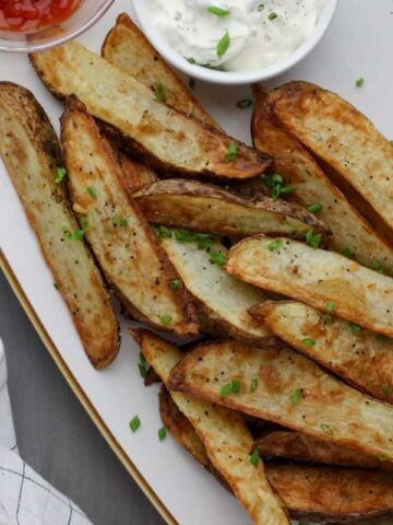 A white platter of crispy air fryer steak fries sprinkled with chives.