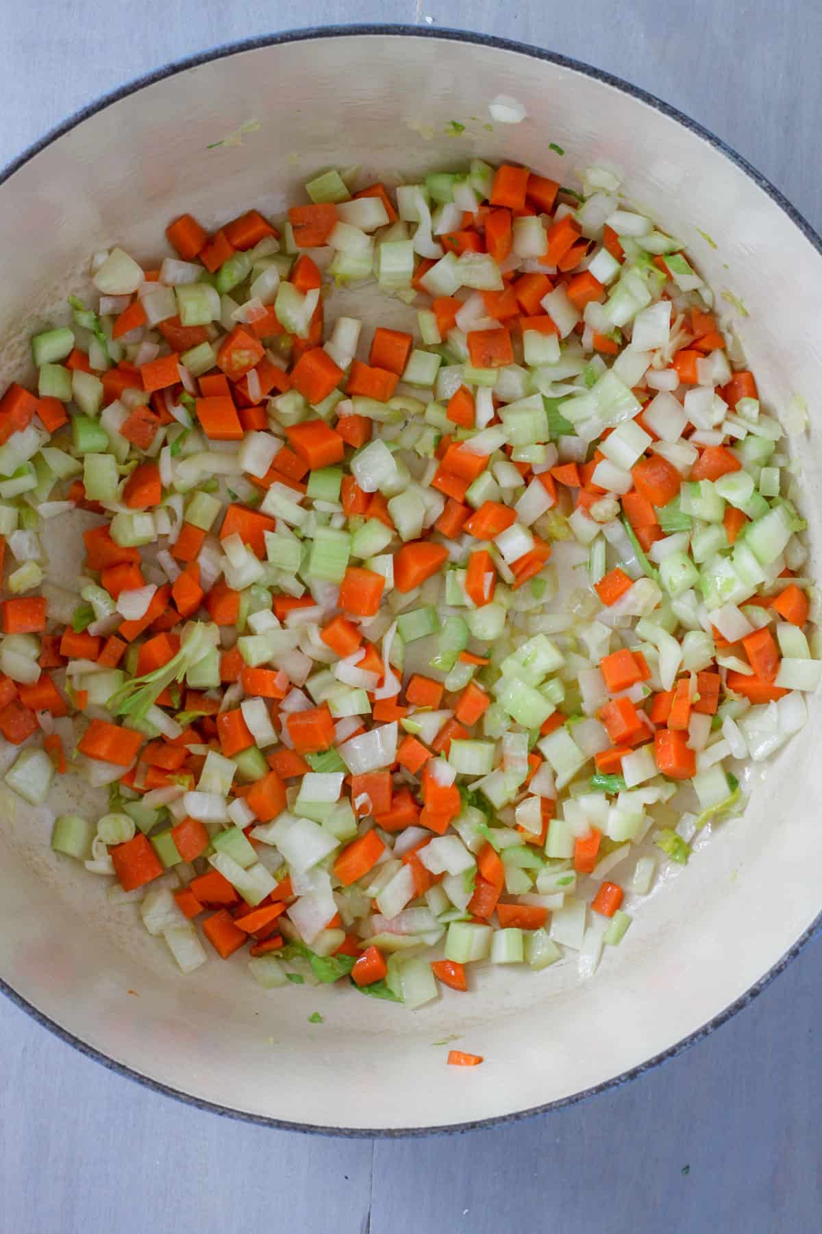 A Dutch oven with onion, celery and carrots cooking.