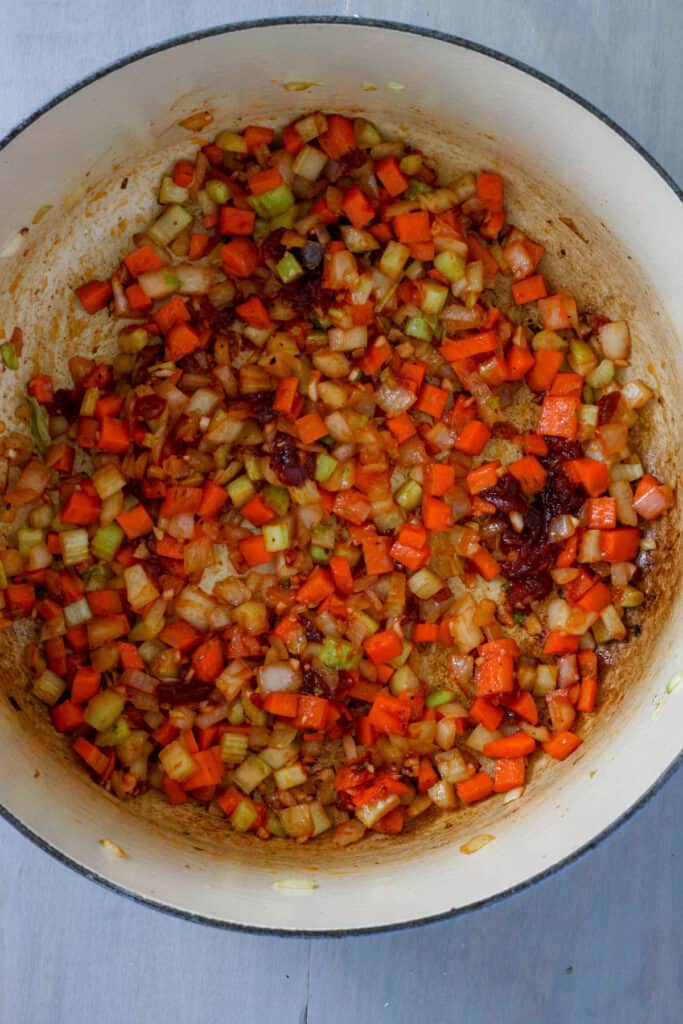 A Dutch oven with onions, celery, carrots, tomato paste, garlic and tomato jam.