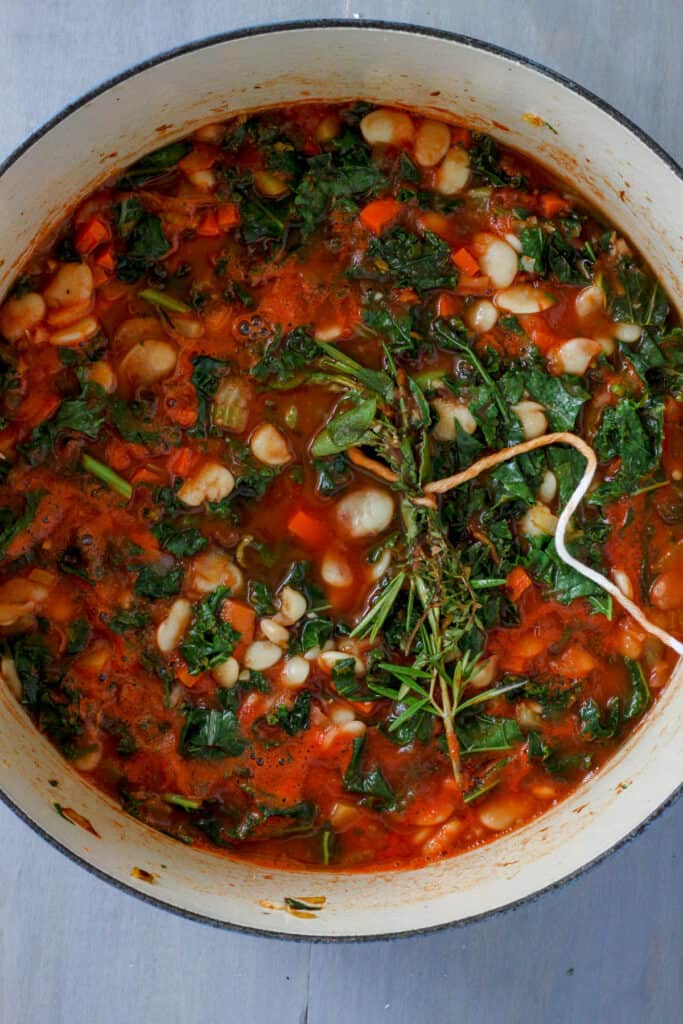 A Dutch oven with butter bean stew simmering and a bouquet garni inside.