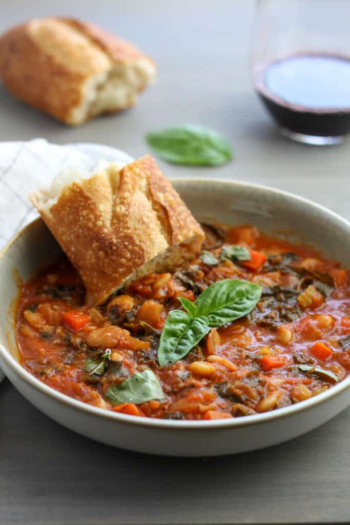 A bowl of butter bean and kale stew with basil and crusty bread on top.