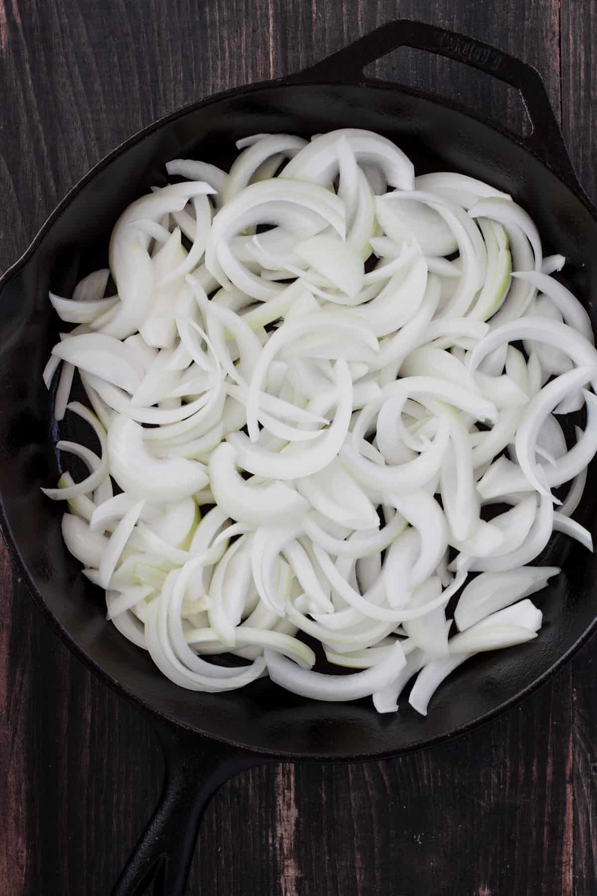 Sliced sweet onions in a large cast iron skillet.