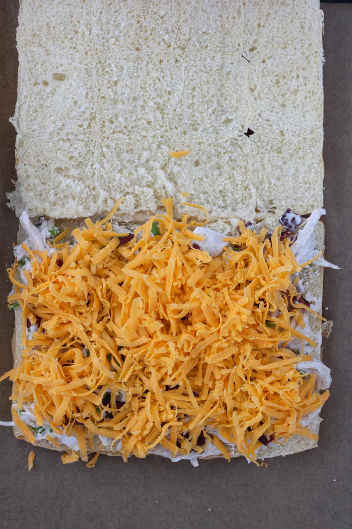 Chicken bacon ranch sliders getting assembled topped with shredded Colby cheese.