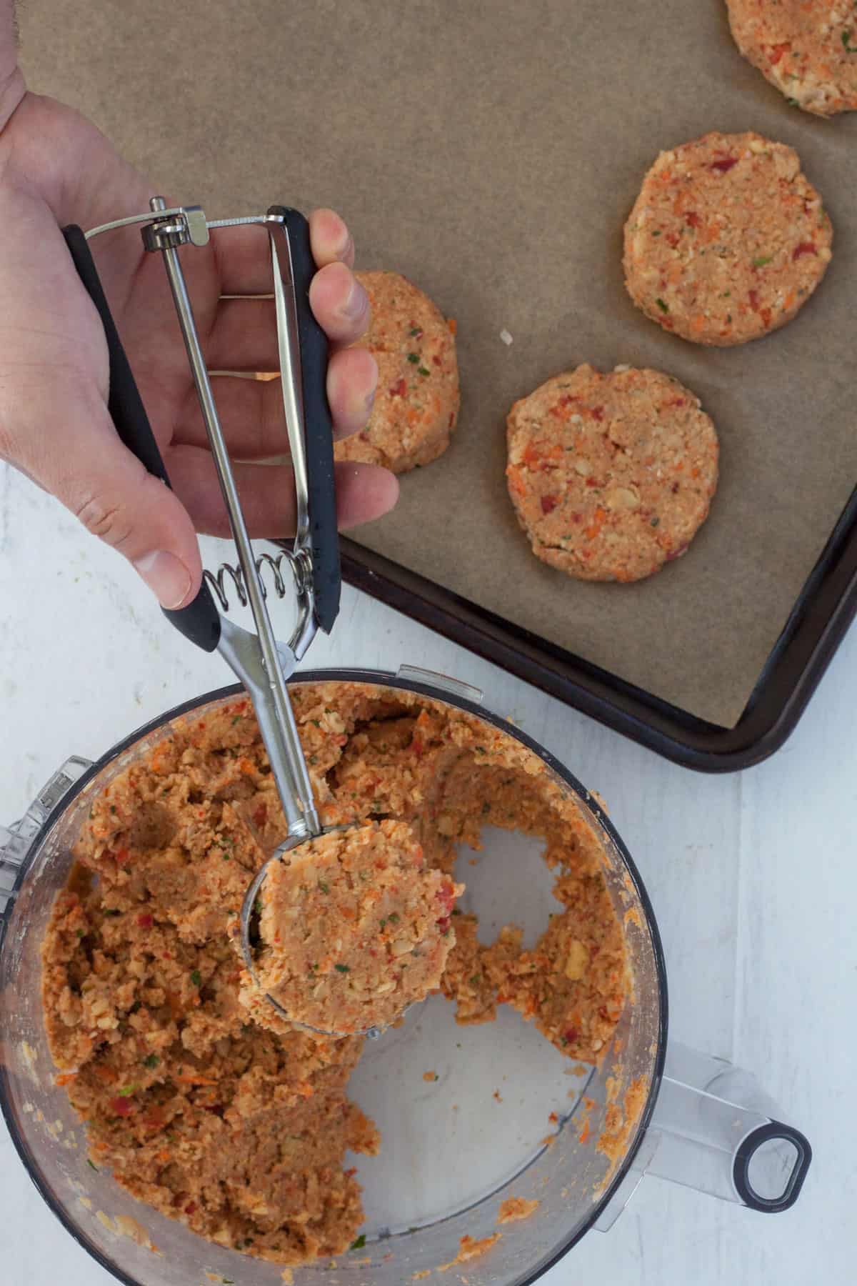 An ice cream scooping taking a scoop of batter for chickpea patties from a food processor.