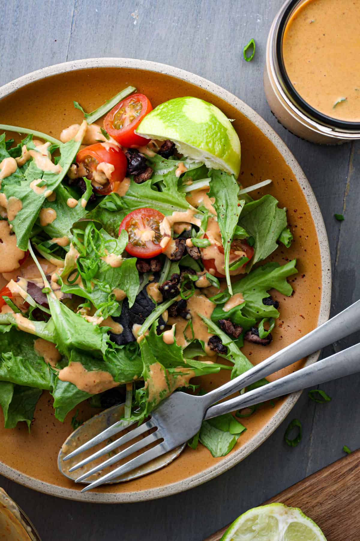 A green salad topped with creamy chipotle lime sauce, chopped tomatoes, lime wedges and roasted black beans.