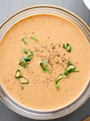 A glass bowl with creamy chipotle lime sauce topped with fresh scallions.