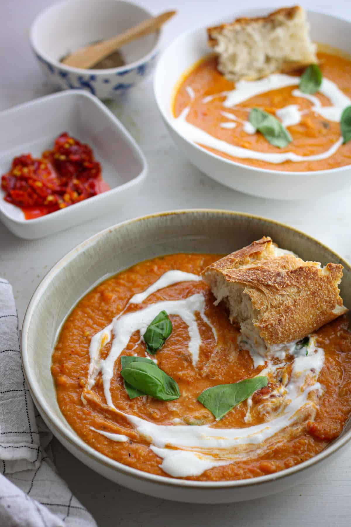 A bowl or lentil and red pepper soup topped with yogurt and basil and served with crusty bread.