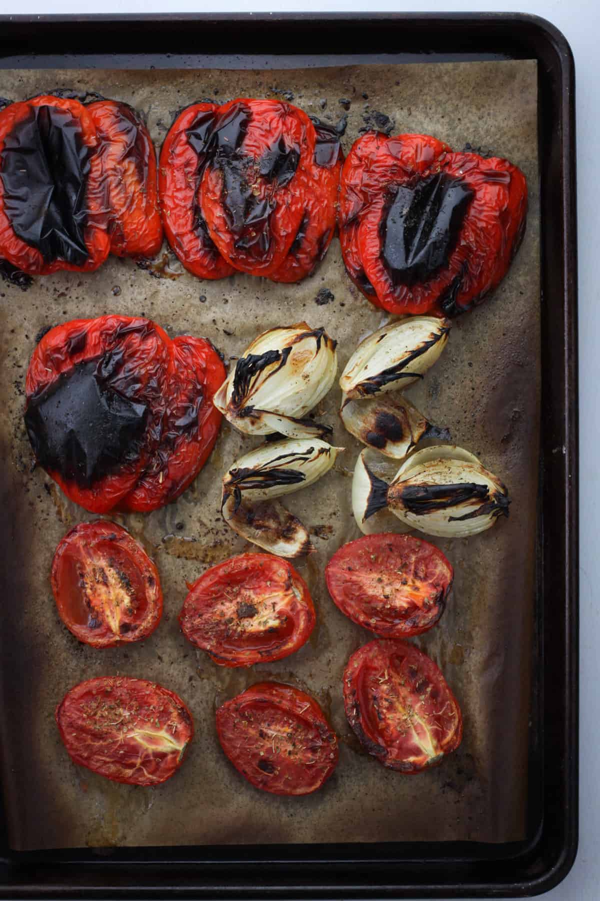 A sheet tray with roasted red peppers, charred onions and roasted Roma tomatoes.