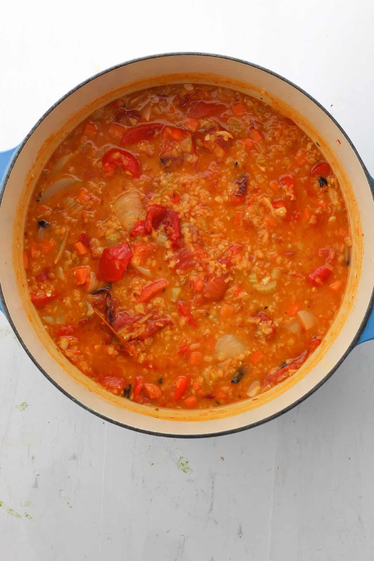 A Dutch oven with lentil and red pepper soup cooking.