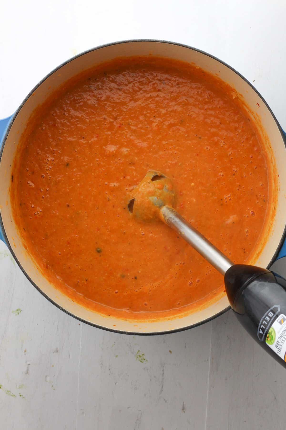 A Dutch oven with pureed lentil and red pepper with an immersion blender partially in the pot.