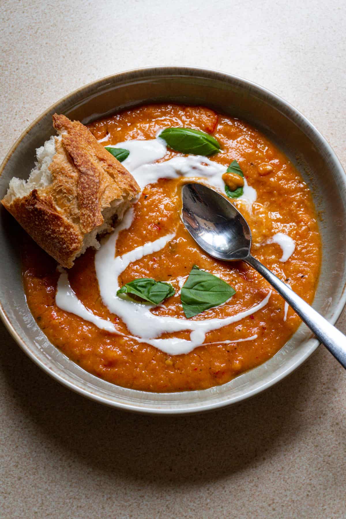 A bowl of lentil and red pepper soup topped with yogurt, fresh basil and crusty bread.