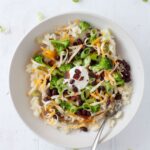 A loaded potato bowl topped with shredded cheese, black beans, scallions and more.
